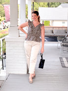 Woman standing on a porch wearing a patterned top and beige pants, holding a black handbag.