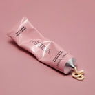 Pink tube of hand balm with cream oozing out on a pink background